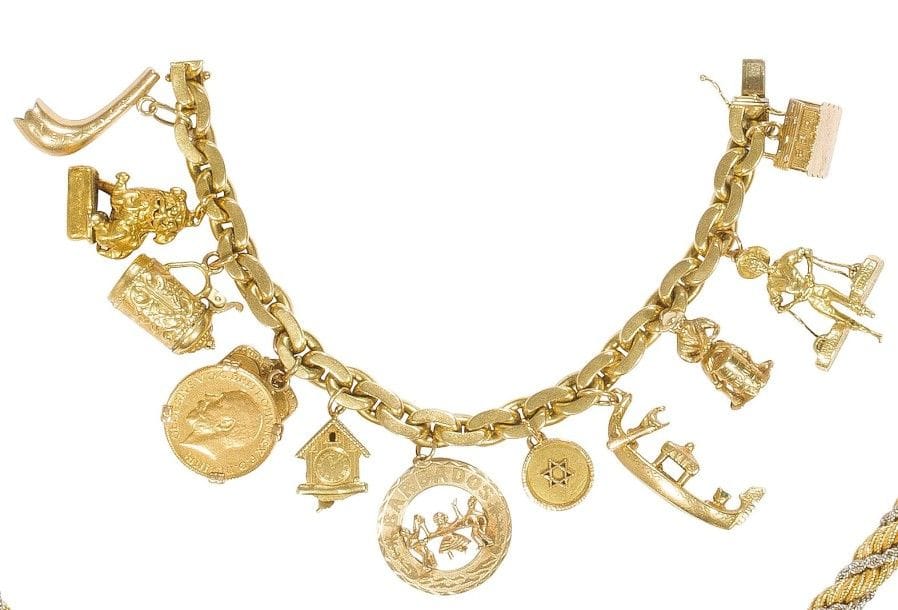 Bracelet en or jaune 18K (750‰), retenant en pampilles 12 breloques en or : un chalet, un paysan portant ses paniers, un joueur de tambour, une gondole (signée Nardi), une médaille ornée d’une étoile de David, un pendentif souvenir de la Barbade (14K), un coucou suisse (18K), une pièce à l’effigie de George V, un pendentif représentant les Tables de la Loi (18K), une chope, un chien de Fô, un shofar. 
Poids brut : 123 g
