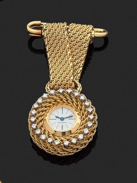 CARTIER. Montre-broche en or jaune cordé 18K (750‰), cadran rond entouré de diamants, montée sur deux rubans d’or retenus par une épingle à nourrice, mouvement mécanique. Numérotée. 
Diam. : 2,5 cm environ. Haut. : 5,5 cm environ. 
Poids brut : 33,8 g