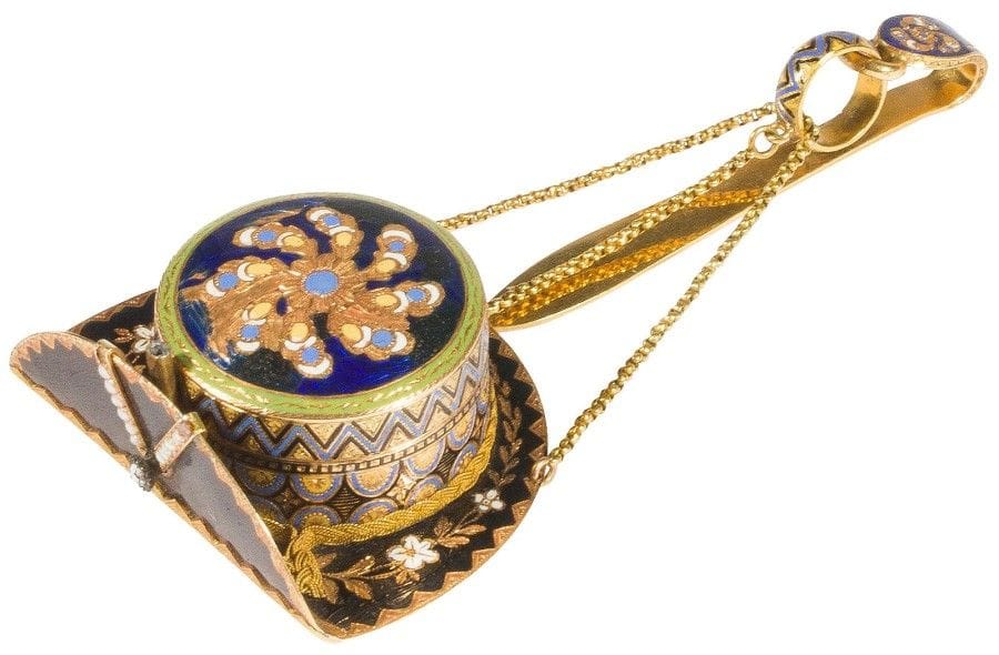 Très originale montre de poche en or 18K (750‰) stylisant un chapeau à bord relevé, ornée d’émaux polychromes dessinant des fleurs et des feuillages, agrémentée de petites perles et d’une rose, le fond formant un miroir dans un décor émaillé polychrome ; retenue par 3 chaînettes à un crochet en or. 
Travail du XIXe siècle. Mécanisme à coq non signé.
Poids brut : 27,80 g
Accident à l’émail.