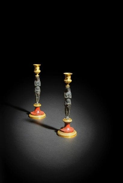 Paire de flambeaux aux égyptiennes en bronze patiné, doré et marbre rouge griotte, la figure d’égyptienne les bras croisés soutenant une bobèche ornée de godrons, reposant sur un piédouche en marbre et bronze doré à décor guilloché et perles.
Fin du XVIIIe - début du XIXe siècle.
H : 28,5 cm

Une paire de flambeaux présentant de grandes similitudes, le piédouche entièrement en bronze doré et la bobèche à feuillages et fruits a été vendue à New York chez Christie’s les 29 et 30 Novembre 2012, lot 1.