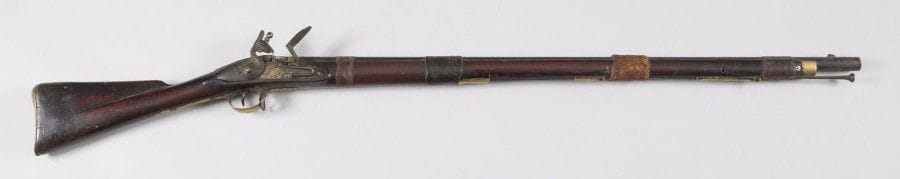 Fusil à silex dit « de traite ». 
Canon rond patiné maintenu par des bracelets en peau. Platine marquée « TOWER » et chien à corps rond. Garnitures en laiton patiné. Crosse en noyer verni. 
E.M. (Accident). XIXe siècle. 