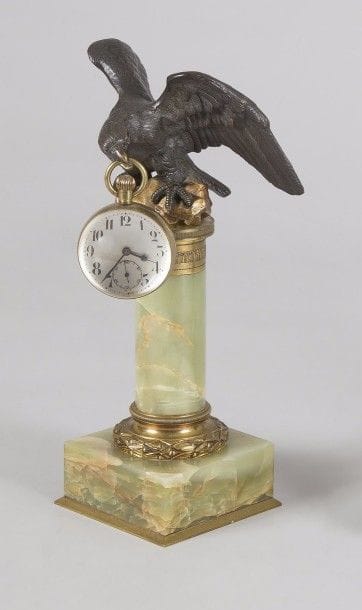 « L’Aigle » 
Porte-montre en laiton patiné sur colonne et socle en onyx. Avec sa montre globe à monture en laiton et cadran émaillé à chiffres arabes. 
Hauteur : 34 cm 
B.E. 
