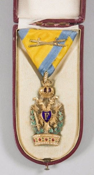 AUTRICHE
ORDRE DE LA COURONNE DE FER, modifié en 1816. 
Insigne de 3e classe, à titre militaire, à couronne de lauriers. 
Bronze doré et émail. Ruban triangulaire à motif d’épées entrecroisées.
Poinçon à l’étoile et du fabricant sur l’anneau. 
Dans son écrin marqué. 
T.T.B. 