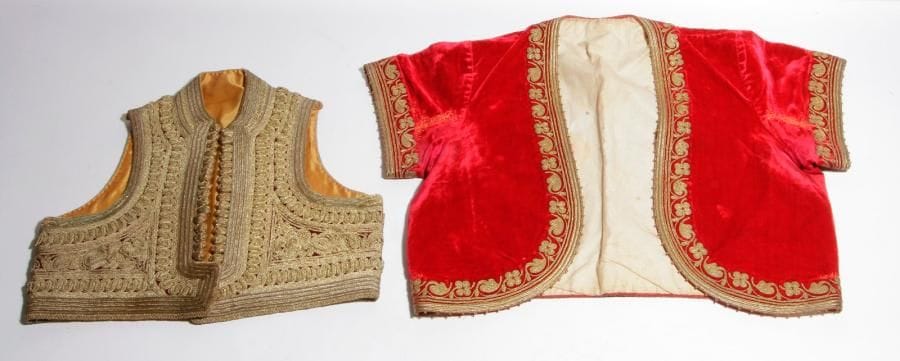 »Deux gilets de femme ou d’enfant « Jelek » :
- En velours, entièrement et profusément brodé de galon doré à décor d’entrelacs. Faux boutons brodés de fil doré orné de corail. 
- En velours écarlate (réparation), brodé de frise de fleurs en fil et galon doré. Doublure en toile blanche et rouge. 
B.E. 