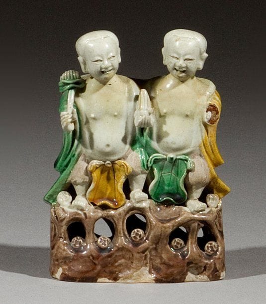 CHINE. Epoque Kangxi (1662 - 1722)
Groupe en porcelaine émaillée jaune, vert et manganèse sur le biscuit, les deux frères Hoho debout sur un rocher et tenant des pièces de monnaie. On y joint deux statuettes de chimères, l'une avec son petit, l'autre debout. (Accidents et manques, restaurations). Hauteurs : 14 et 14,5 et 8,5 cm