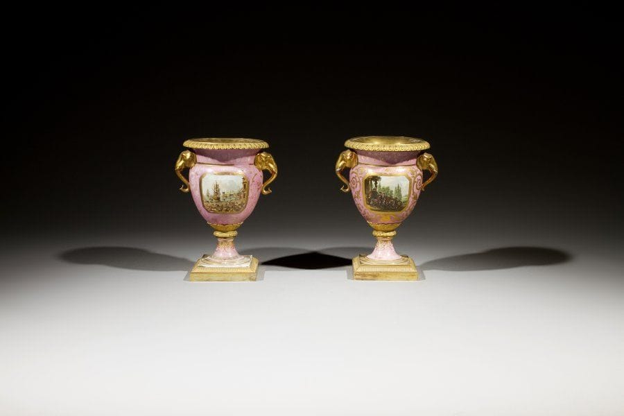 Grande paire de vases à fond vieux rose à décor dans des réserves sur deux faces de scènes portuaires ou de paysages animés de cavaliers. Les anses ajourées en forme de têtes d'éléphants. Montures de bronze ciselé et doré à prises de feuilles d'eau, palmettes et godrons. Vers 1830. Fausse marques de Sèvres. (Usures, éclats et restaurations). Hauteur : 36,5 cm - Largeur : 29 cm