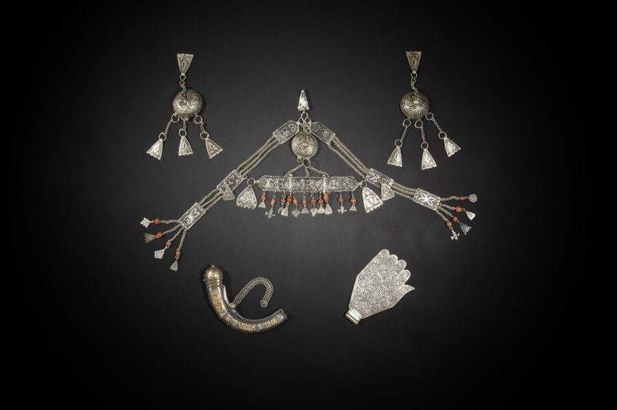 Parure de tête en métal, Maroc, Moyen Atlas, Aït Sehrouchen, XXe siècle
Diadème constitué de trois plaques articulées à décor floral gravé et niellé à pendeloques de perles de corail, reliées par des chaînettes à des pendants de tempes et à un crochet de soutien. Joint un pendant d'oreille niellé à tête hémisphérique et pendants en triangles.
Dim. parure : 25 x 41 cm 

A head ornament, Morocco, Moyen Atlas, Aït Sehrouchen, 20th century
