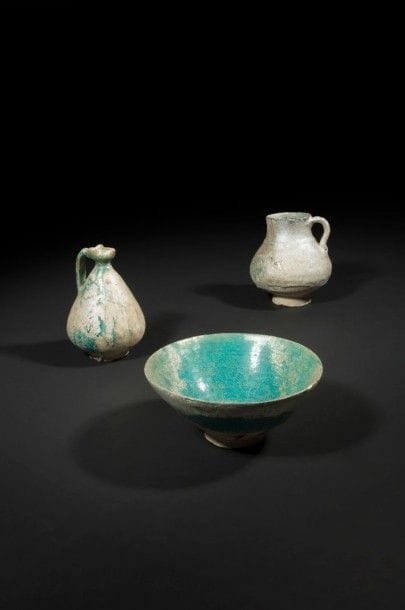 Trois céramiques turquoises, Iran XIIe - XIIIe siècle
Deux pichets en céramique siliceuse glaçurée turquoise, l’un à panse conique légèrement godronnée, à bec tréflé avec anse ; l’autre à panse globulaire, col droit et anse en esse ; une coupelle à bords évasés sur base circulaire et traces d’incisions sur la panse. 
Haut. pichets : 6 cm, 5,4 cm ; diam. coupelle : 7,5 cm, haut. : 8 cm 
État : fortes irisations, manque au bord pour la coupelle et à la base pour les pichets. 
Two blue glazed pottery jugs and a bowl, Iran, 12th - 13th - century 