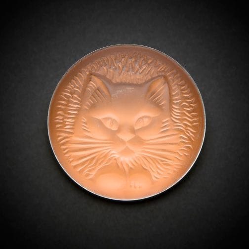 Maison LALIQUE d’après un modèle de Marie-Claude LALIQUE (1935-2003)
Tête de chat 
Broche en cristal moulé-pressé, achevé satiné, sur tain miroir orange. Platine en métal argenté. Signée LALIQUE au revers. D. 4,8?cm
