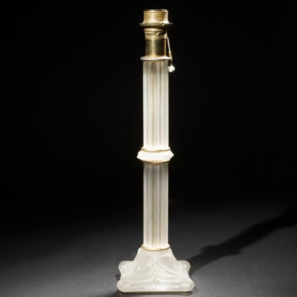 Maison LALIQUE d’après un modèle de Marie-Claude LALIQUE (1935-2003)
Olympie, modèle créé en 1981
Pied de lampe. Épreuve en cristal moulé-pressé satiné, les bagues en métal doré (Réf. Catalogue général Lalique 2012 pages 184 & 185). Un infime éclat et égrenures sur la base, usures à la dorure des bagues. Signé LALIQUE®France à la pointe sur la tranche de la base. H. 48,5?cm (avec douille)
