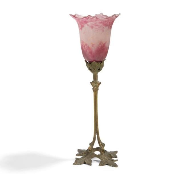 TRAVAIL ART NOUVEAU & DAUM Nancy
Pied de lampe en bronze patiné au décor feuillagé. Tulipe rapportée, à l’évocation d’un volubilis, en verre marmoréen rose et blanc. Montage non d’origine. La tulipe signée DAUM Nancy à la Croix de Lorraine en intaille (lecture inversée). H. totale?: 41?cm
