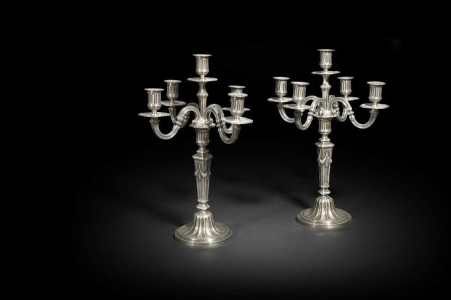 Paire de bougeoirs en bronze argenté à cinq bras de lumière de style Louis XVI, le piédouche à cannelures en rappel sur les binets, le fût à pans agrémenté de lauriers en chutes.
H  : 45,5 cm - D : 14,4 cm
