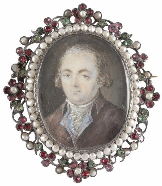 Portrait d’homme en costume marron, gilet bleu brodé de rose et jabot de dentelle,
Miniature ovale (à vue 4,8 x 3,1 cm) sur une broche en argent à épingle en or, entourée de demi-perles et d’une guirlande de fleurettes en argent ajouré serti de perles et grenats, XIXe siècle, ovale H. totale 6 x 5,3 cm