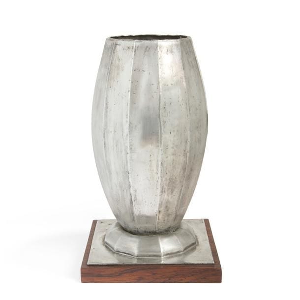Jean DESPRÉS (1889-1980)
Rare vase moderniste en dinanderie d'étain.
Le corps ovoïde facetté repose sur un talon en doucine facettée accueilli par une base carrée.
Terrasse en palissandre.
Enfoncements épars.
Signé J. DESPRÉS sur la base en étain.
Hauteur avec terrasse : 38,5 cm
Provenance :
Ancienne Collection M. et Mme X., anciens propriétaires du Buffet de la gare à Avallon - France, œuvre acquise par ces derniers directement auprès de l'artiste.
Œuvre en rapport :
Une œuvre très proche est reproduite sur une photographie d'archive, montant Jean Després dans son atelier, publiée dans l'ouvrage de Melissa Gabardi - Jean Després, maestro orafo tra art deco e avanguardie - édité par Idea Books en 1999.