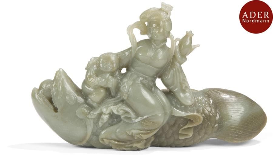 CHINE - XXe siècle
Groupe en néphrite céladon, jeune femme et enfant assis sur une carpe, et tenant une verseuse.
Longueur : 22 cm
