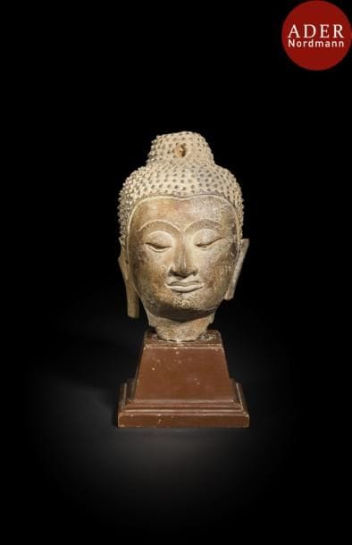 THAÏLANDE, Ayutthaya - XVIIIe siècle
Tête de bouddha en bronze à patine brune, les yeux mi-clos, la coiffe finement bouclée et surmontée de son chignon. (Accidents).
Hauteur : 16 cm
Socle en bois.