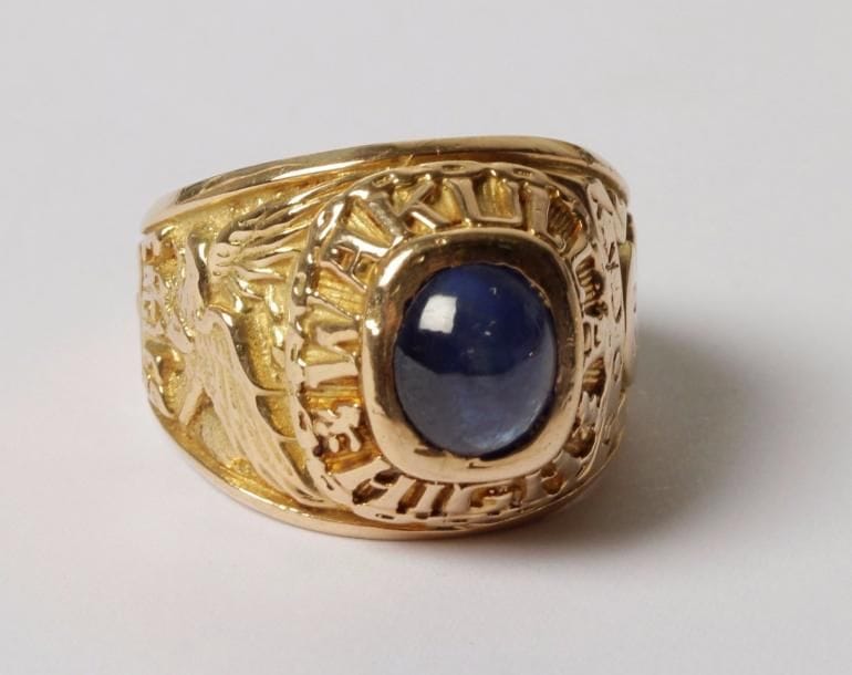Bague américaine de fin d’études en or 14K (585‰), ornée d’un saphir cabochon et gravée d’inscriptions.
Tour de doigt : 62. Poids brut : 21,8 g
