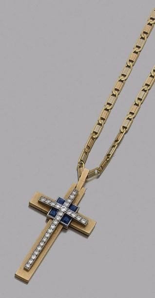 Pendentif croix en or 18K (750‰), orné de diamants sur platine et de 5 saphirs calibrés, coulissant sur une chaîne d’or 18K.
Hauteur : 4 cm environ. Poids brut : 18 g