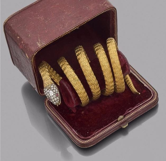 Bracelet armille en or 18K (750‰) tressé formant un serpent, la tête pavée de diamants taillés en roses, les yeux soulignés d’un rubis cabochon. Dans son coffret en cuir.
Travail de la fin du XIXe - début du XXe siècle.
Poids brut : 45,2 g