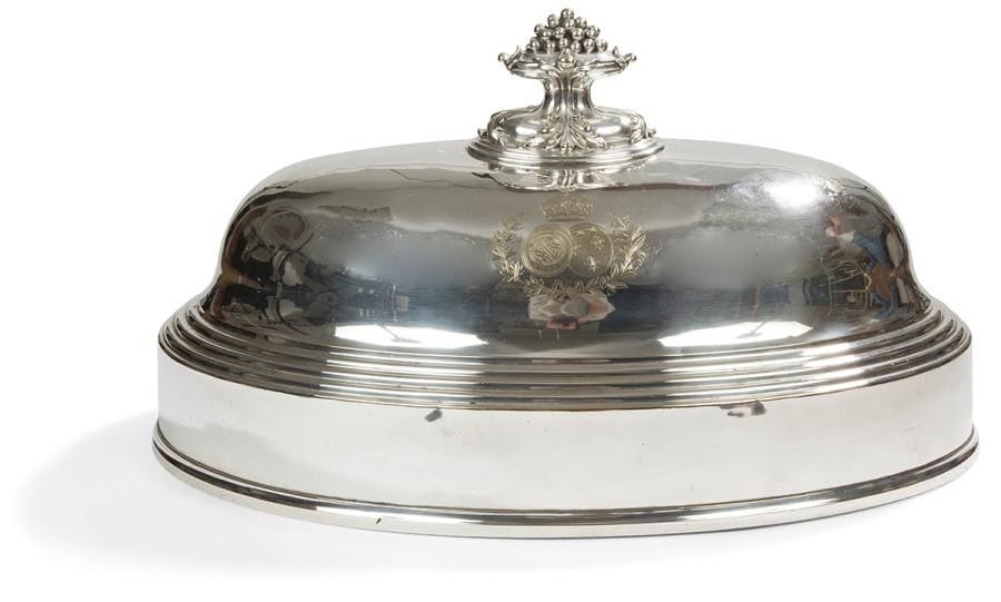 Importante cloche à gradins en métal argenté de forme ovale, la prise amovible terminée par une corbeille de fruits. Elle porte les armes d’alliance ORLEANS / BRAGANCE consacrant le mariage en 1864 à Rio de Janeiro d’Isabelle, fille de l’Empereur Pierre II du Brésil et de Gaston d’Orléans, petit-fils de Louis-Philippe.
État d’usage : restauration ancienne, faiblesse à l’argenture
France, 1864 - 1865
Orfèvre : CHRISTOFLE
Porte le  numéro : 514669
Longueur : 52,5 cm - largeur : 35 cm - hauteur : 29,5 cm
Nous remercions Anne Gros qui nous a communiqué la date de fabrication de cet objet.
