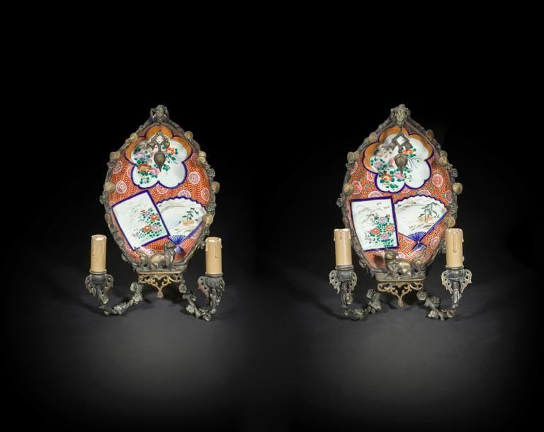 Paire d’appliques à deux lumières en porcelaine, bronze doré et bronze patiné dans le goût de la Chine, à décor de chimère, coquilles, fleurs, feuillages et grelot.
Attribuée à la maison l’Escalier de Cristal.
XIXe siècle (usures).
H : 36 cm, L : 23,5 cm