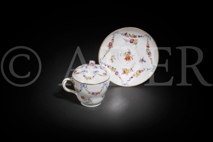 Meissen
Tasse couverte et sa soucoupe en porcelaine à décor polychrome de guirlandes de fleurs retenues par des rubans bleu noués.
Marqué : épées croisées et étoile en bleu.
Période de Marcolini.
XVIIIe siècle, vers 1780.
H. 10 cm, D. 13 cm
Usures au centre de la soucoupe et éclat à la prise du couvercle