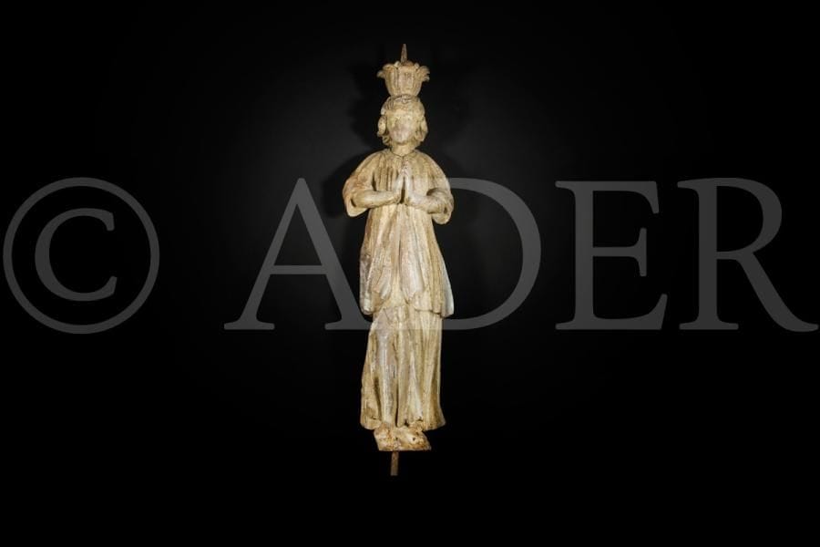 Pique-cierge en forme de personnage en bois sculpté en ronde-bosse et monochromé. Debout, les mains jointes, il porte sur sa tête un bouton fleuri muni qu’une pique ; il est vêtu d’une robe fendue sur le genou droit et d’une tunique ouverte sur le devant ; visage ovale encadré par une chevelure abondante aux mèches ondulées. 
Début du XVIIe siècle
Hauteur : 53,5 cm
