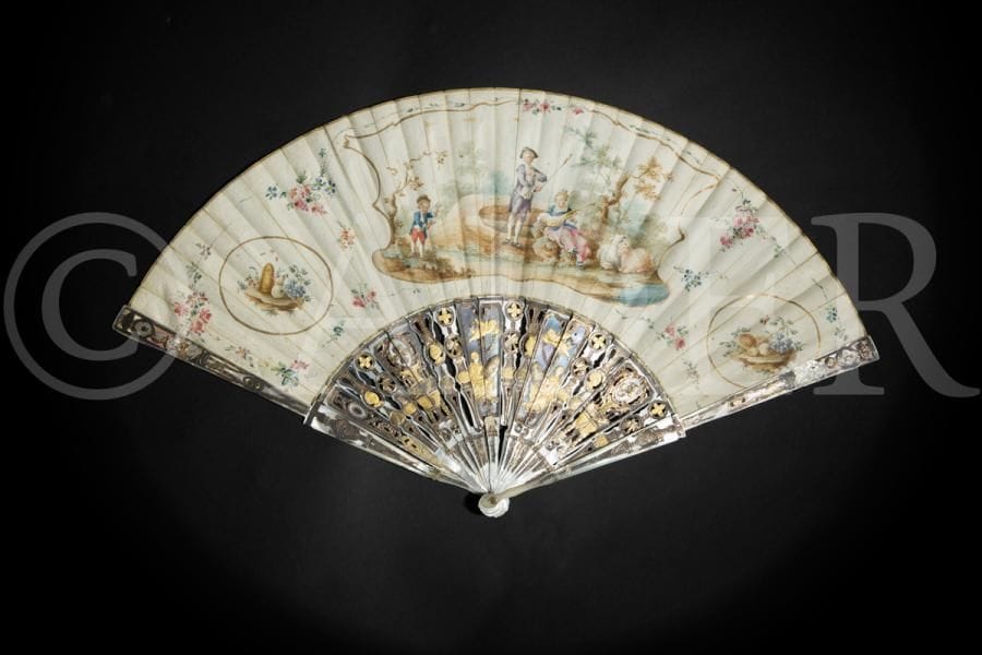 Eventail en velin peint et ivoire ajouré, argenté et doré, à décor de scènes galantes dans des réserves à entourages de branchages fleuris ; dans un coffret d’époque postérieure.
XVIIIe siècle (accidents).
55 x 30 cm