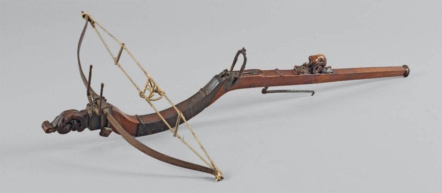 Arbalète à jalet. Arbrier mouvementé, travaillé à pans, en bois fruitier (cerisier), sculpté sur le dessus d'une femme dénudée et, à l'avant, de feuillages. Arc, mécanisme et garnitures en fer forgé. Avec sa corde à panier en corde tressée, à écarteur en bois et prise en cuir. Italie. XVIIe siècle. Ancienne réparation à l'avant par plaque de métal en renfort, cassure sur la partie arrière. Longueur : 100 cm. Envergure : 55,8 cm