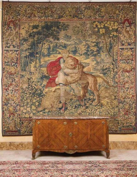 Tapisserie de Bruxelles. XVIIe siècle. En laine et soie représentant un des douze travaux d'Hercule : Hercule terrassant le lion de Némée. On peut voir Hercule à l'oeuvre en train de terrasser le lion, entouré d'autres lions dans un paysage de verdure et de forêts représentant la vallée de Némée. La tapisserie est terminée par une très importante bordure où figurent des animaux sauvages et des volatiles, le tout dans un décor de pergolas fleuries dans le plus pur style de l'époque. Cette scène représente donc le premier travail d'Hercule. Il était le fils de Zeus et d'Alcméne. Marié à Mégara qu'il tua dans un accès de folie. Pour expier ce crime la Pythie l'envoya auprès du roi de Tirynthe, Eurysthée, qui lui imposa une série d'épreuves «les douze travaux d'Hercule» dont le premier était de tuer le lion de Némée. Némée était une vallée de L'Argolide (Péloponése) sur la route de Corinthe à Argos où il existait un lion qui terrorisait la population. C'est donc cette scène qui est représentée sur cette tapisserie. 350 x 360 cm