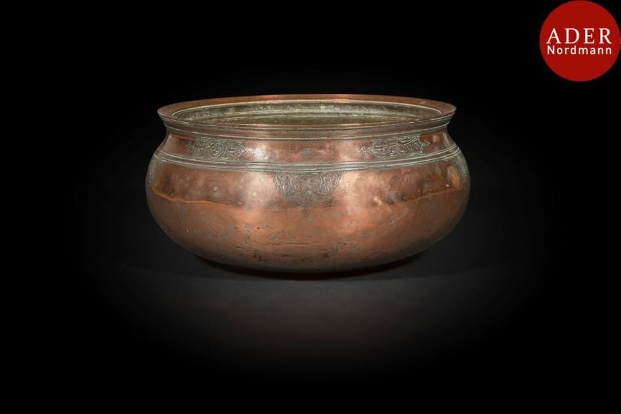 Grand bassin en cuivre, Iran, daté 1745 
Panse globulaire à col incurvé orné de cinq cartouches de poésie persane, quatrain, et nom de propriétaire : 
« Que cette coupe soit toujours pleine de bien-être / Que tout ce que tu en manges soit bénéfique pour ta santé.
Il faut que tu exprimes la gratitude pour le bien-être / Qu’on accorde au possesseur de cette nourriture la miséricorde. 
Son propriétaire est Ahmad b. Muhammad Tavvâf Astarâbâdi ».
Au rebord supérieur, un texte en persan mentionne un Shâh Mansur et la date en mot et en chiffre de 1158H. / 1745-46. 
Diam. : 31 cm ; haut : 16 cm 
Astrabâd ou Astarâbâd est une ville iranienne située à une trentaine de kilomètres au sud de la mer Caspienne, actuellement Gurgân, capitale de la province du Golestan. 
A large copper bowl, Iran, dated 1745