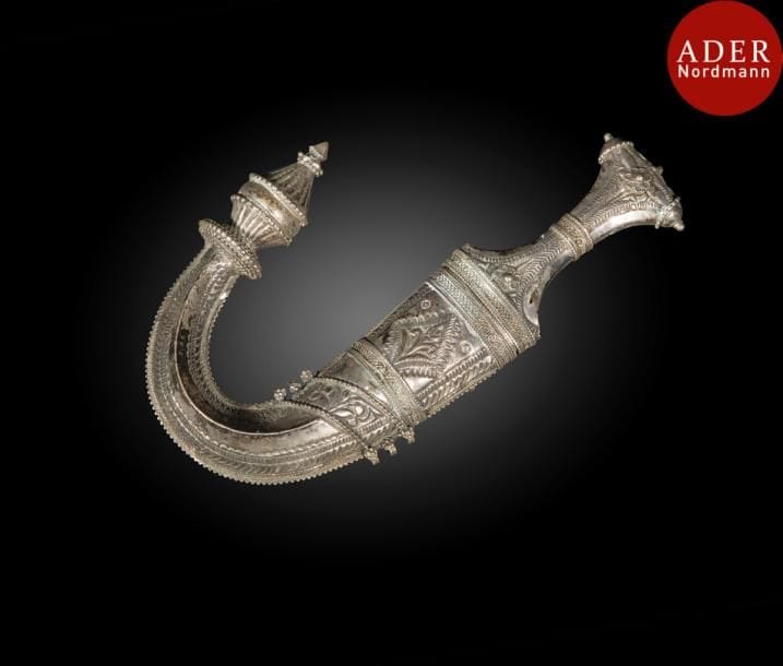 Poignard, jambiya, Yemen, XXe siècle 
Lame courbe en acier à ricasso, monture et fourreau en métal filigrané et ciselé de frises géométriques et florales. Sept anneaux d’attache.
Long. : 27,3 cm
État : taches brunes
An Arabian horn-hilted dagger, jambiya, Yemen, 20th century 