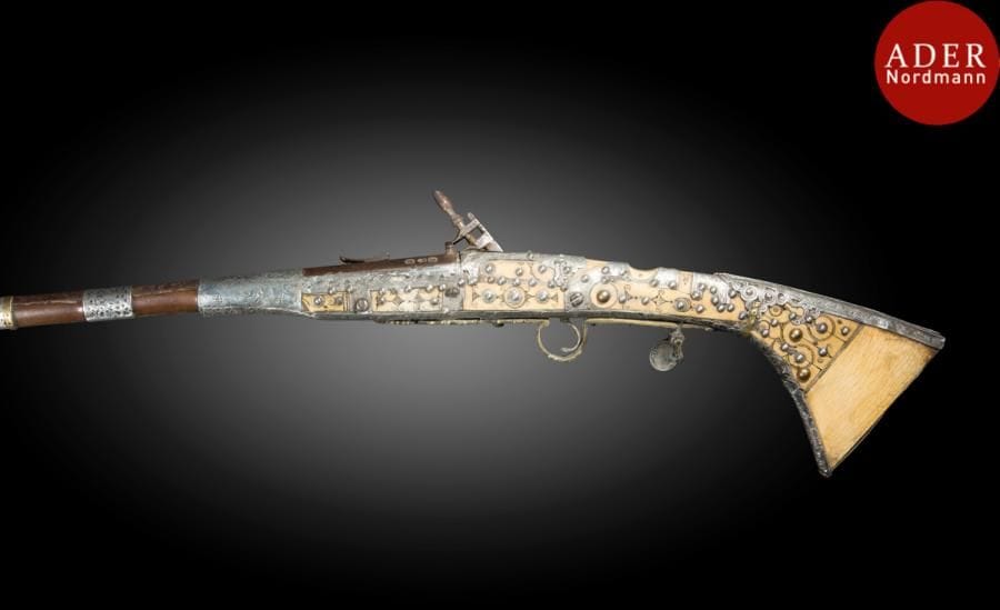 Fusil à silex, mukhala, Afrique du Nord, signé et daté 1869
Long canon en bois à bagues d’argent dont certaines ciselées de fleurs, crosse en os, à garnitures d’argent ciselées de rinceaux et cloutées. Baguette. Sous la platine, inscriptions donnant le nom du fabricant « Mohammad ibn al-Hossein al-Zeyd » et la date « mois de Chavval 1286 H. / 1869 »
Long. : 162 cm
A flintlock pistol, mukhala, North Africa, signed and dated 1869