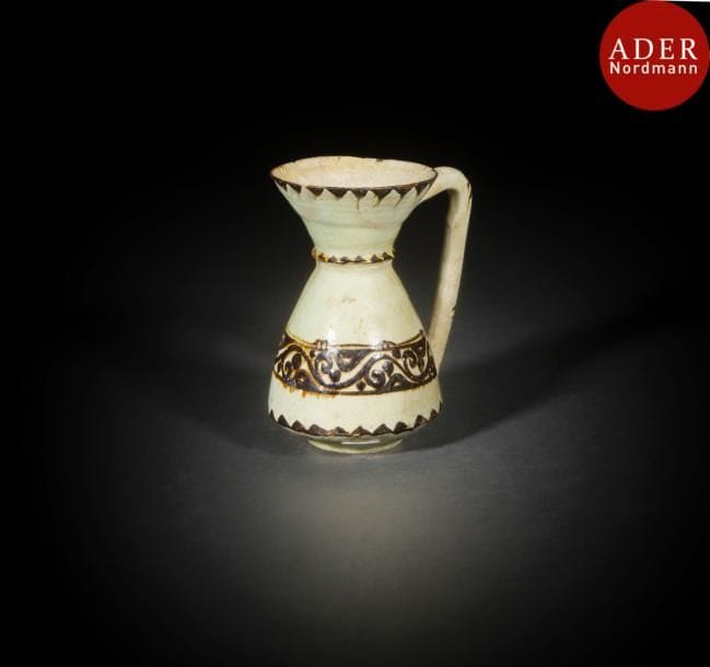 Pichet en céramique, Iran oriental, Nishapur, XIe-XIIe siècle
Céramique argileuse à panse piriforme, col évasé et anse coudée, peinte en brun sur fond crème d’un registre d’entrelacs végétaux à la panse et de frises de triangles à la base et au col. 
Haut. : 16.5 cm
État : restaurations
A Nishapur pottery pitcher, Oriental Iran, 11th-12th century