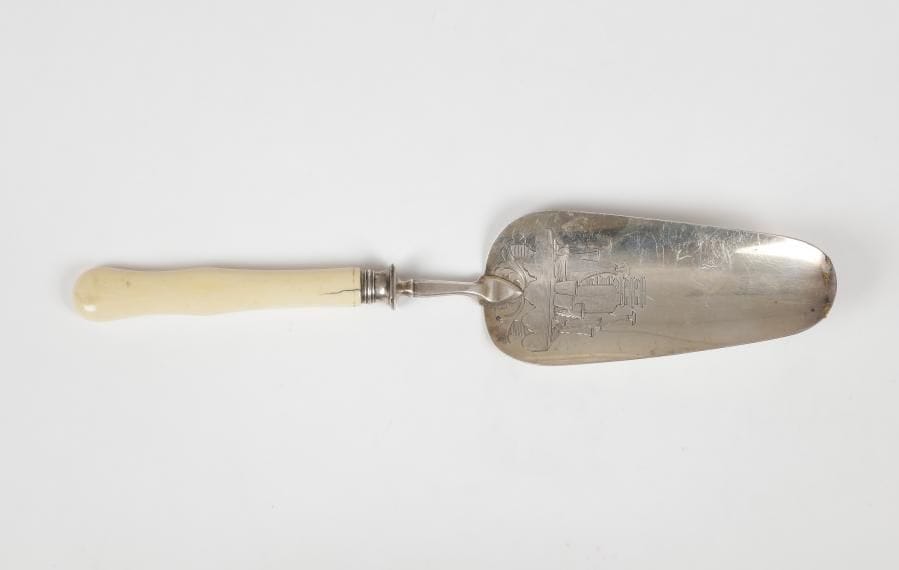 Amusante pelle à gâteau en argent manche en ivoire (fêle), gravée de la représentation d'une table sur laquelle sont posés bouteille, carafes et verres.Poinçon minerve
Poids brut : 98 g - longueur : 28,2 cm