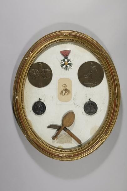 Cadre reliquaire contenant les souvenirs de Camille GUILLIER de la TOUCHE, maire d’Angers. 
Il comprend : 
- étoile de chevalier de la Légion d’honneur d’époque IIe République. Argent, or et émail (éclats). Ruban.
- deux médaillons en laiton d’après David d’Angers commémorant le sacrifice des 4 sergents de la Rochelle. 
- deux médailles en argent de député, attribuées pour les années 1848 et 1849. Diamètre : 4,5 cm 
- une photographie carte de visite. 
- cuillère et couteau artisanaux utilisés lors de sa captivité à Vincennes après 1851. 
Encadré sous-verre bombé. 