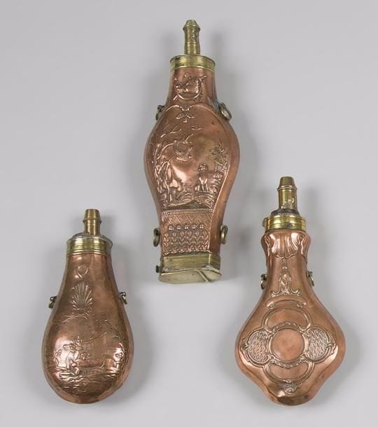 Trois grandes poires à poudre dont une en cuivre estampé, à bec en laiton.
Deux possèdent un décor cynégétique et une est à décor de rinceaux. 
L’une possède également un rangement pour les balles, à quatre anneaux de suspente. 