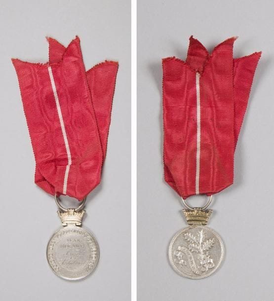 FRANCE 
Médaille de la Société des volontaires de 1870-1871, à la branche de houx. 
En argent, gravée « Jean MUGNIER – Service des Ambulances ». Long ruban à liseré blanc. 
Hauteur : 3,6 cm - Poids brut : 13 g 
T.T.B.