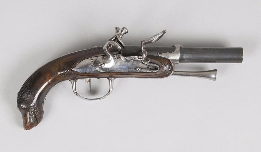 Pistolet d’officier de marine. 
Canon rond à méplats au tonnerre. Platine et chien col de cygne à corps ronds. Bassinet en fer. 
Garnitures, crochet de ceinture et baguette en fer. Crosse en noyer joliment sculpté d’une tête de « chien de mer ». 
B.E. Vers 1770 / 1780.