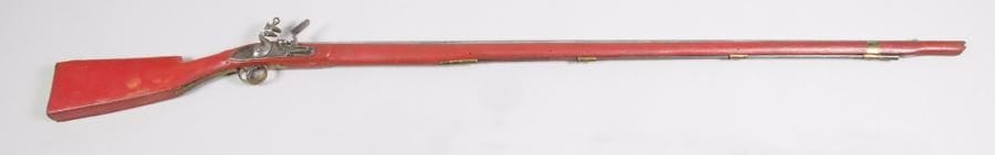 Fusil à silex « perroquet » dit de braconnier.
Canon rond à pans au tonnerre. Platine à corps plat et chien à corps rond. Garnitures en laiton, unies. Fût et crosse peints en rouge. Baguette en fer. 
B.E. XIXe siècle.
N.B.: ces fusils étaient peints de couleurs vives, (rouge, jaune, vert), pour surprendre et faire des échanges avec les indigènes.