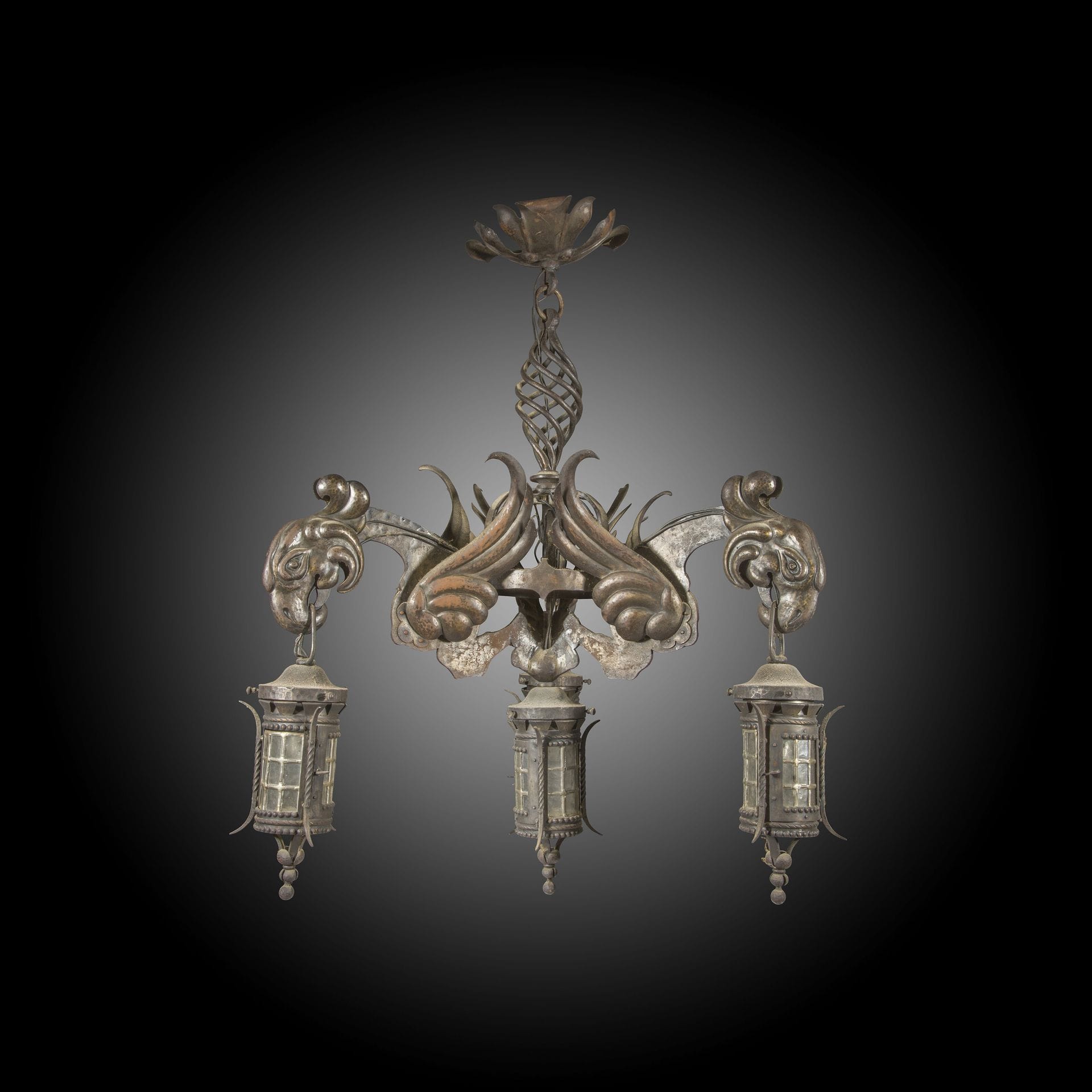 Curieux lustre en fer battu et tôle patinée de goût néogothique, à quatre lanternes chinoises dont trois tenues par des becs de perroquets, les bras ailés réunis à un fût ajouré à torsades en spirale.
Probablement Angleterre, fin du XIXe siècle
D : 80 cm
