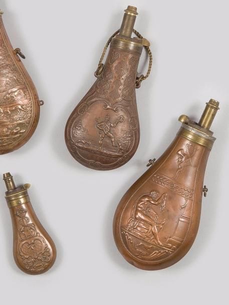 Trois poires à poudre :
- une grande en cuivre estampé marquée « VIVE LA JOIE ». Bec doseur gradué, en laiton.
- une grande en cuivre estampé à décor antique. Signée « BA A PARIS ».
- une petite poire à poudre de boîte à décor rocaille.
B.E. XIXe siècle. 