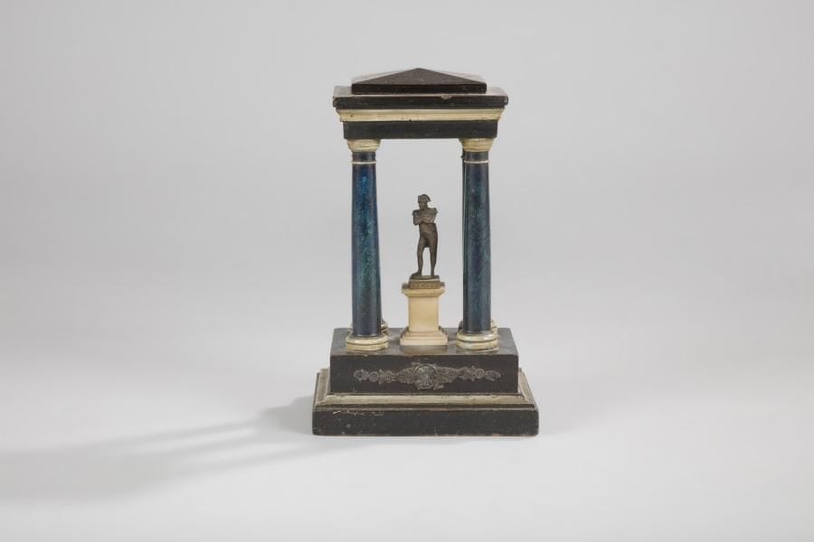 À la gloire de l’Empereur Napoléon Ier
Porte-montre en bois polychrome, à décor de temple antique, présentant une statuette de l’Empereur Napoléon Ier en laiton doré. .
Statuette : 8 cm - Hauteur totale : 29 cm
A.B.E. (manque le crochet de suspension)
Époque Retour des Cendres. 