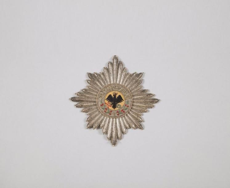 ALLEMAGNE (PRUSSE)
ORDRE DE l’AIGLE NOIR, fondé en 1701.
Plaque d’habit de Chevalier.
étoile à huit branches rayonnantes en lamé, et fils d’argent.
Centre finement brodé sur fond de fil de moire orangée, d’un aigle couronné tenant un foudre et une couronne de lauriers, en fil noir, vert et rouge. Légende brodée en suite « SUUM CUIQUE » et branches de laurier.
Doublée d’origine en papier. Assez bon état (quelques fils décousus).
Diamètre : 13,1 cm
T.T.B. Première partie du XIXe siècle.

Provenance : Famille Benoist- Mechin