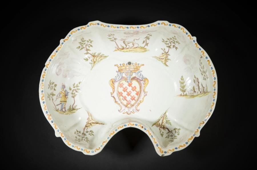 Italie du Nord
Bassin ovale à bord contourné échancré en faïence à décor polychrome au centre d’armoiries dans un écu sous un heaume et une couronne et sur le bord d’animaux fantastiques, soldat et forteresse sur des tertres encadrés d’arbustes.
XVIIIe siècle. 
L. : 37 cm
Légères fêlures, petits éclats et percé pour l’accrochage