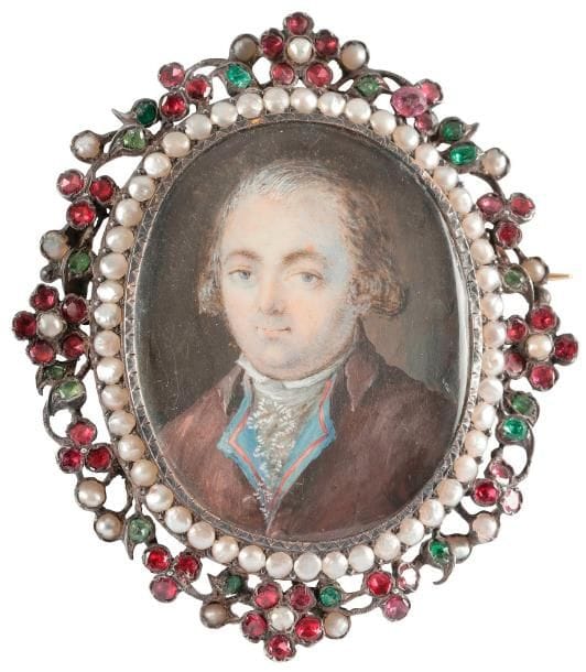 Portrait d’homme en costume marron, gilet bleu brodé de rose et jabot de dentelle,
Miniature ovale (à vue 4,8 x 3,1 cm) sur une broche en argent à épingle en or, entourée de demi-perles et d’une guirlande de fleurettes en argent ajouré serti de perles et grenats, XIXe siècle, ovale H. totale 6 x 5,3 cm