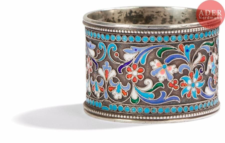 Rond de serviette en argent 88 zolotniks (916 millièmes), à décor émaillé polychrome cloisonné de fleurs et de feuillages stylisés sur fond amati bordés de perles turquoises. Légers sauts d’émail.
Probablement Moscou, 1899-1908.
H. 3,5 x D. 5 cm. Poids brut : 49,14 g

