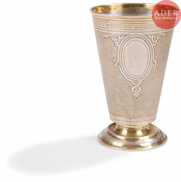 Timbale en argent et vermeil 84 zolotniks (875 millièmes) de forme évasée reposant sur un piédouche, à décor ciselé de deux cartouches non gravés sur fond guilloché de vagues. Bon état, légère usure à la dorure.
Saint-Pétersbourg, 1868.
Orfèvre : SAZIKOV, avec marque de fournisseur de la Cour impériale.
Poids : 108,18 g. H. 10,3 x D. 6,5 cm.

Provenance : À La Vieille Cité, 350 rue St Honoré, Paris (acheté 300 frs dans les années 1950).


