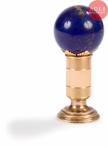 Cachet en or 56 zolotniks (583 millièmes), à décor guilloché et strié, la prise formée par une boule de lapis-lazuli retenue par un motif de godrons en étoile. Le sceau en vermeil est gravé en intaille d’un blason et d’une devise. Bon état, petit choc.
Saint-Pétersbourg, vers 1890.
Orfèvre : Karl FABERGÉ.
H. 6,6 x D. 2,6 cm. Poids brut : 88,60 g
(P Or 10g + P argent : 38 g)
 