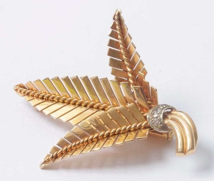 Broche "fougère" stylisée en or 18K (750) ornée d'un lien agrémenté de diamants. Hauteur: 4,6 cm environ. Poids brut: 8,2 g